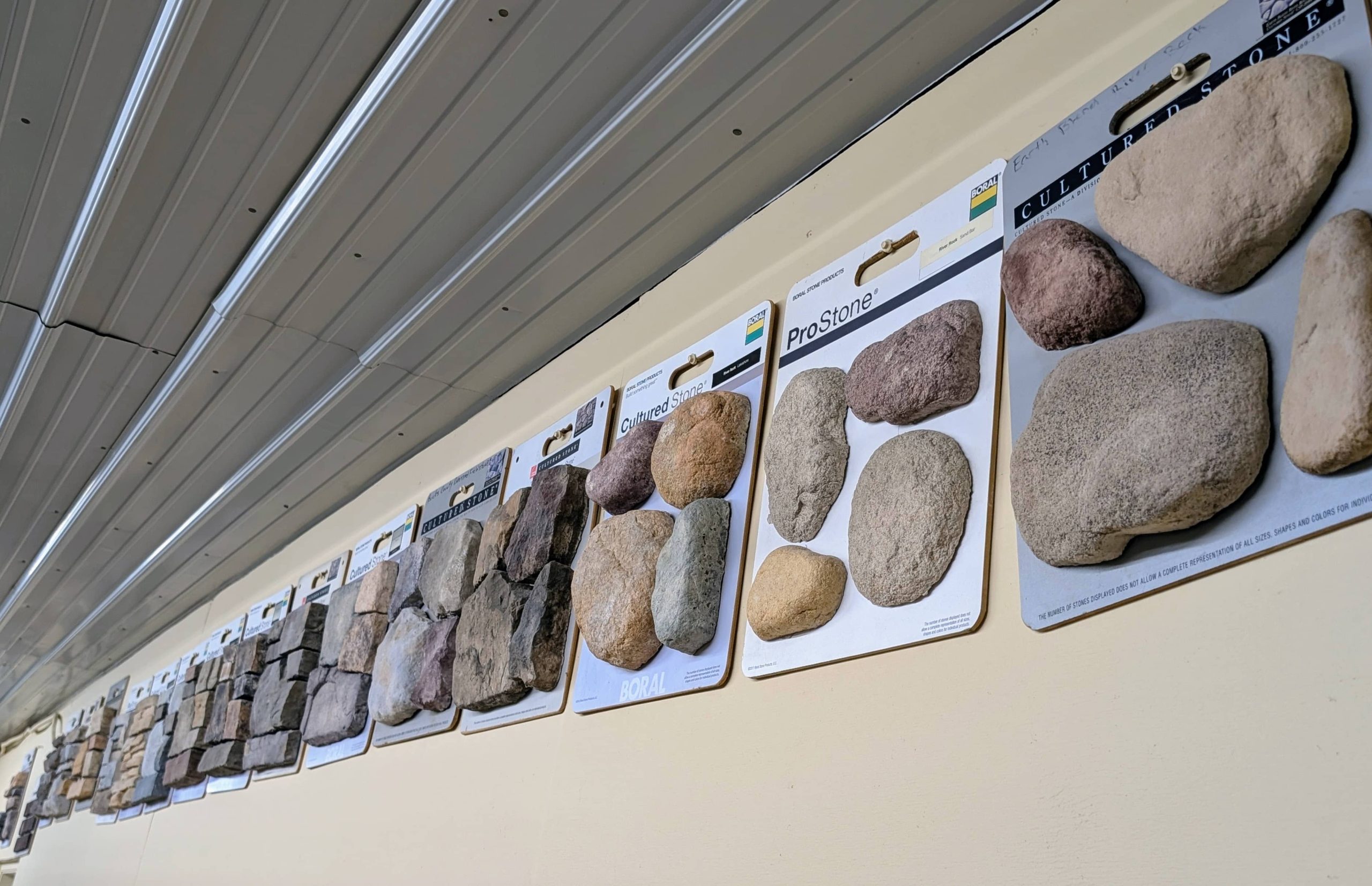 Showroom wall display of Cultured Stone and ProStone sample boards featuring various textures and colors of manufactured stone veneer for fireplace and accent wall applications