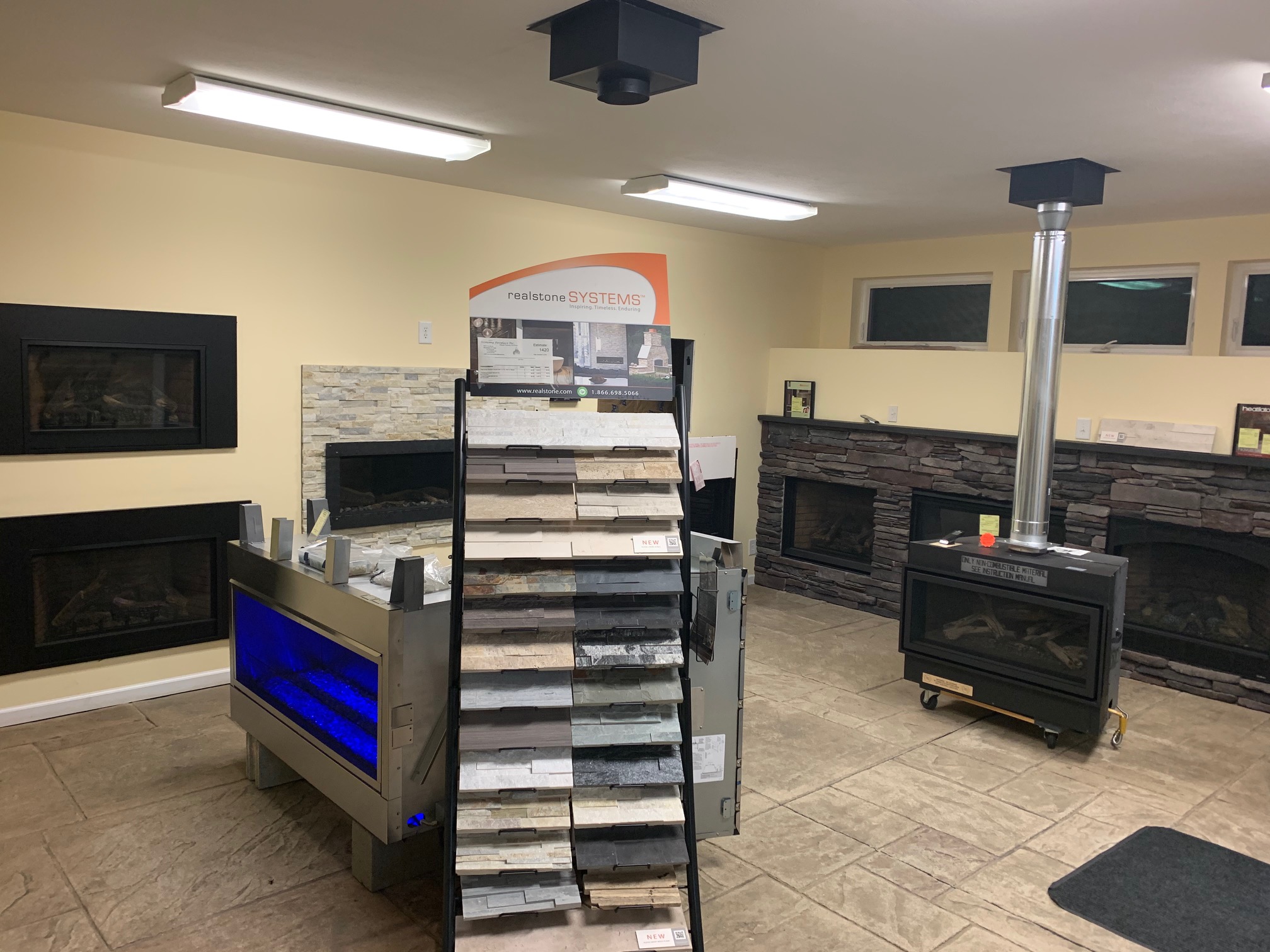 Interior view of the Economy Fireplace showroom featuring various wall-mounted and freestanding fireplaces, a stone veneer sample display, and a modern vented stove unit.