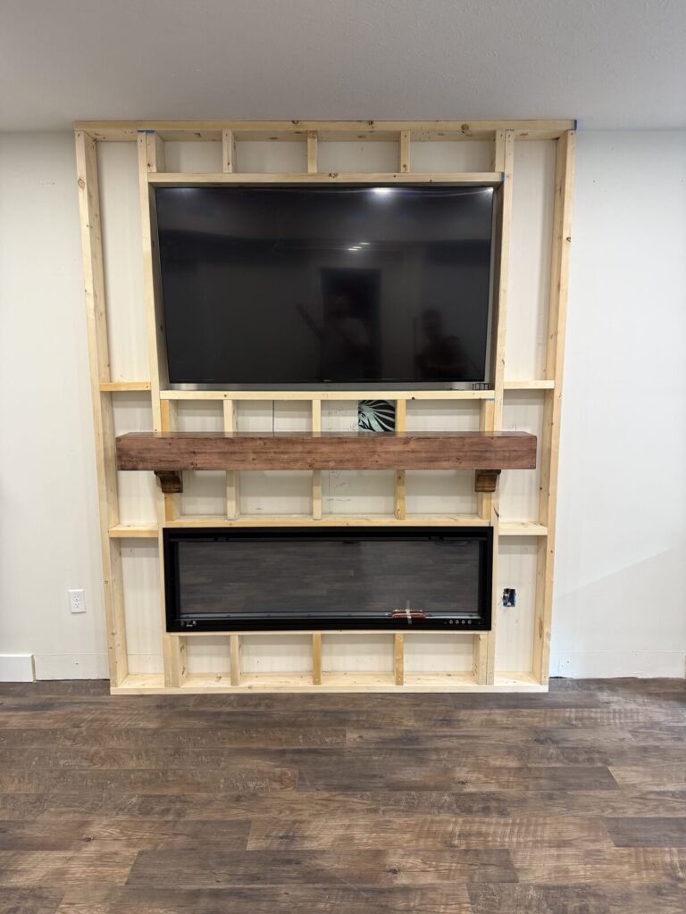 Wall framing with a mounted TV in the recess, a wood mantel beam on corbels, and a 60-inch linear fireplace below