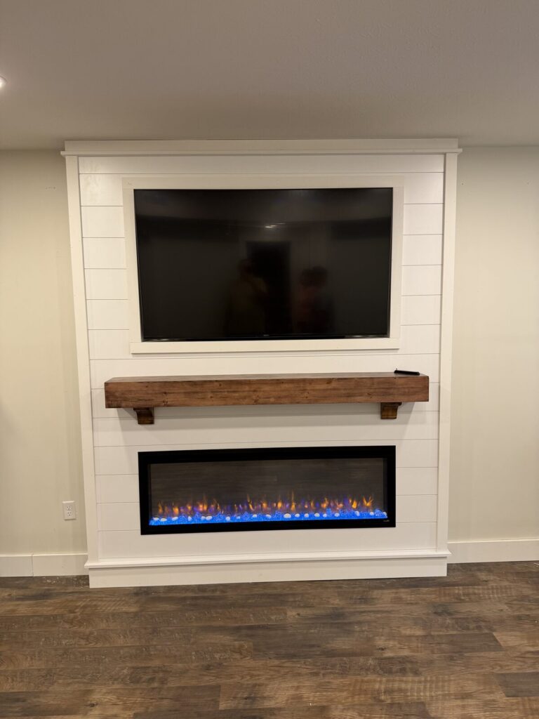 Finished white shiplap fireplace wall with a recessed TV, a stained wood mantel on corbels, and a lit 60-inch linear fireplace below
