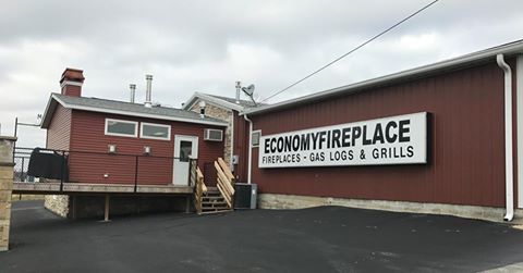 Exterior view of the Economy Fireplace store with red siding, a ramp entrance, and a large sign reading "Economy Fireplace – Fireplaces, Gas Logs & Grills".