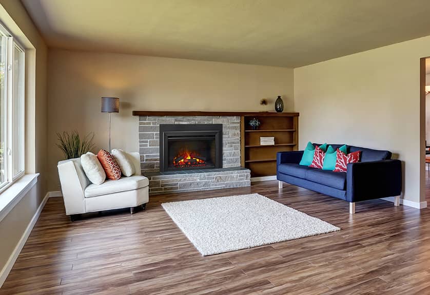 Electric fireplace insert with glowing embers and flame effect, built into a stone mantel in a modern living room with wood floors and mid-century style furniture