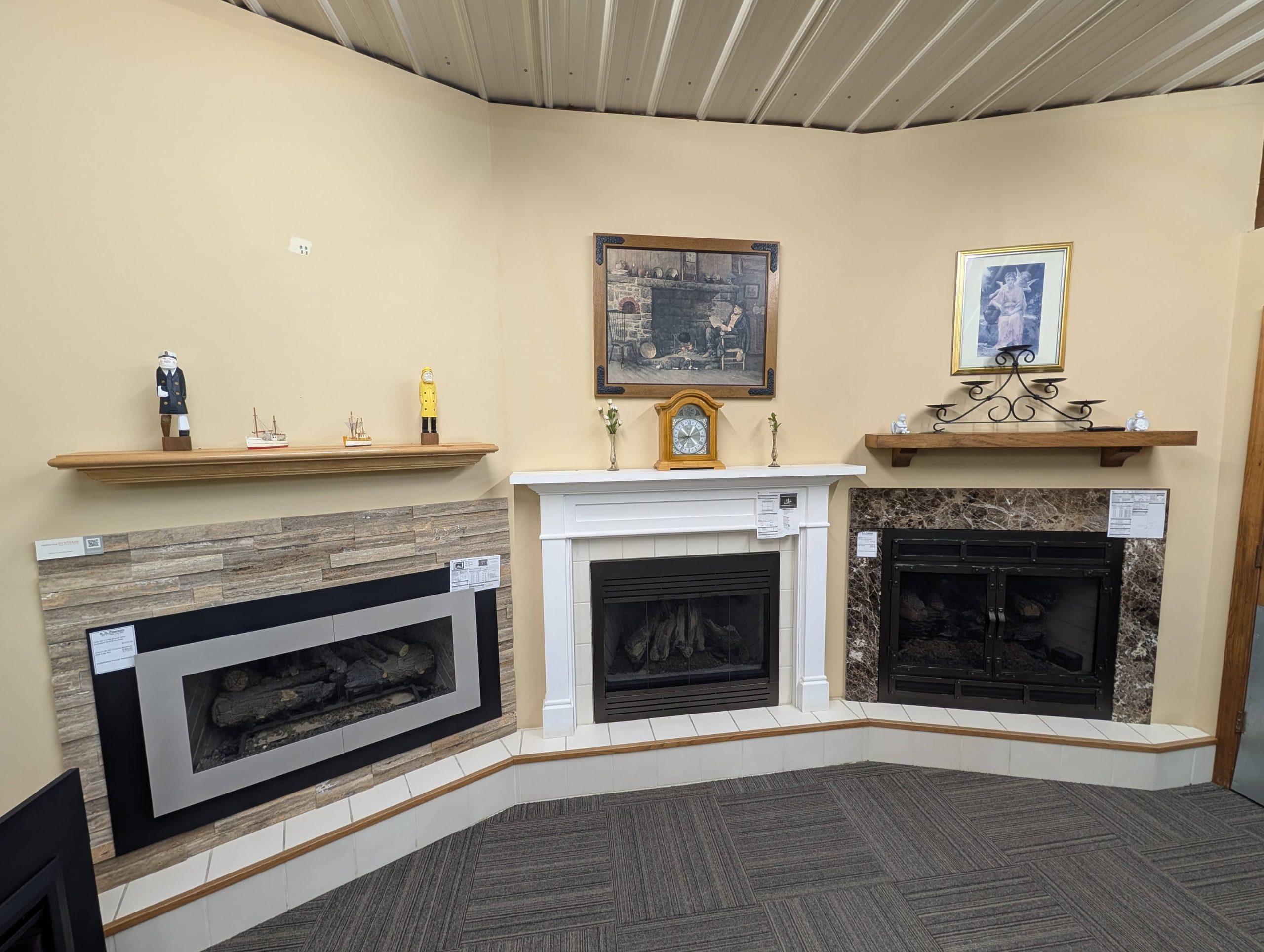 Showroom display of three fireplace setups with varied mantels and wall panels, including modern stone with a sleek frame, white wood mantel, and classic dark marble surround