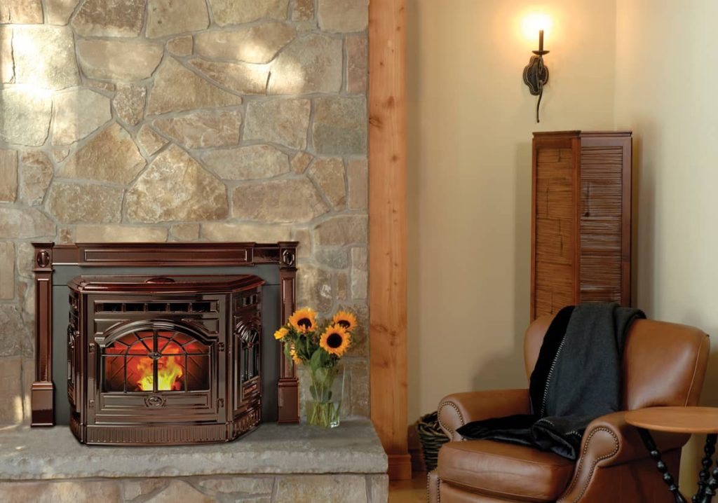 Mahogany-finished Harman pellet fireplace insert with glowing flame, set in a rustic stone surround next to a leather armchair and vase of sunflowers
