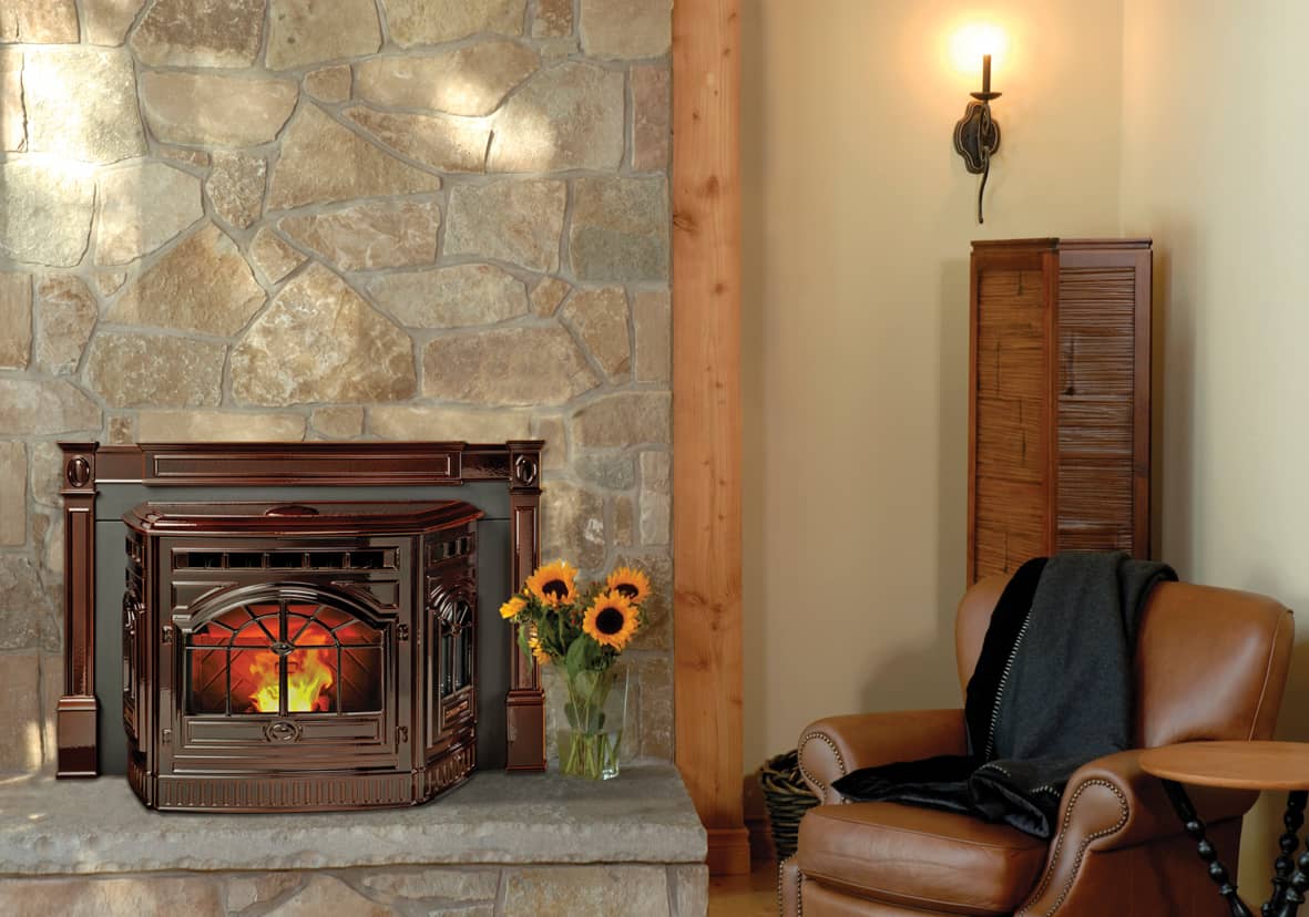 Mahogany-finished Harman pellet fireplace insert with glowing flame, set in a rustic stone surround next to a leather armchair and vase of sunflowers