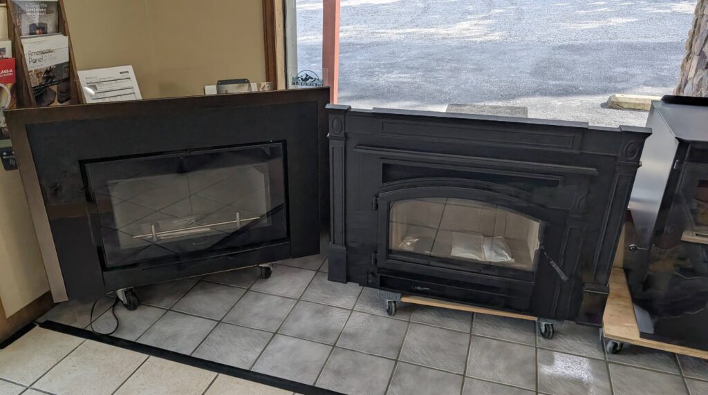 Side-by-side display of two fireplace inserts in a showroom, one with a sleek modern design and the other with a traditional black cast iron style.